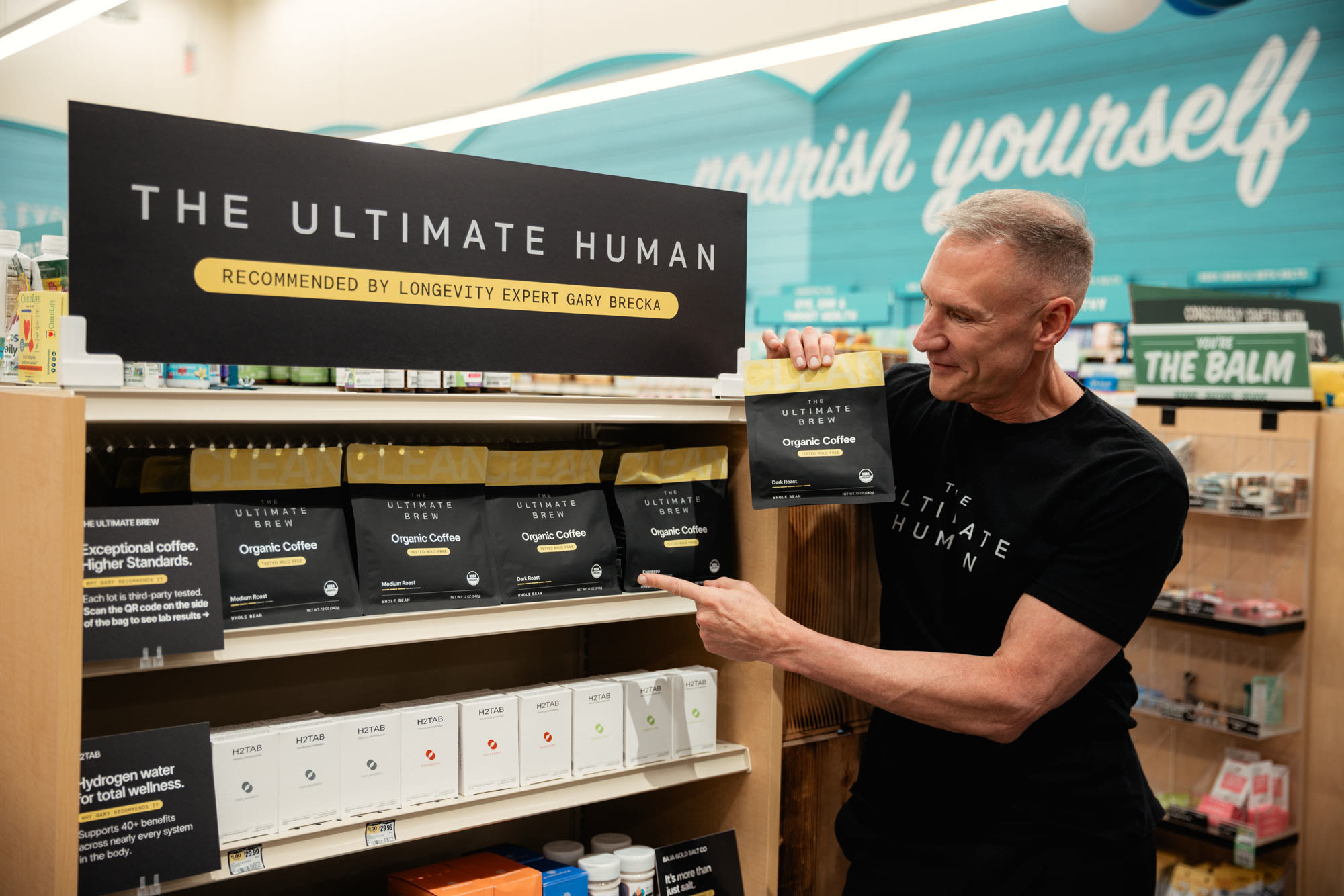Gary Brecka pointing to bags of The Ultimate Brew at the Sprouts endcap