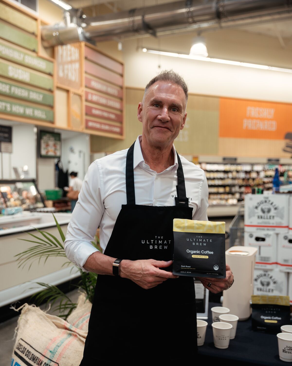 Gary Brecka holding a bag of The Ultimate Brew Dark Roast at the table