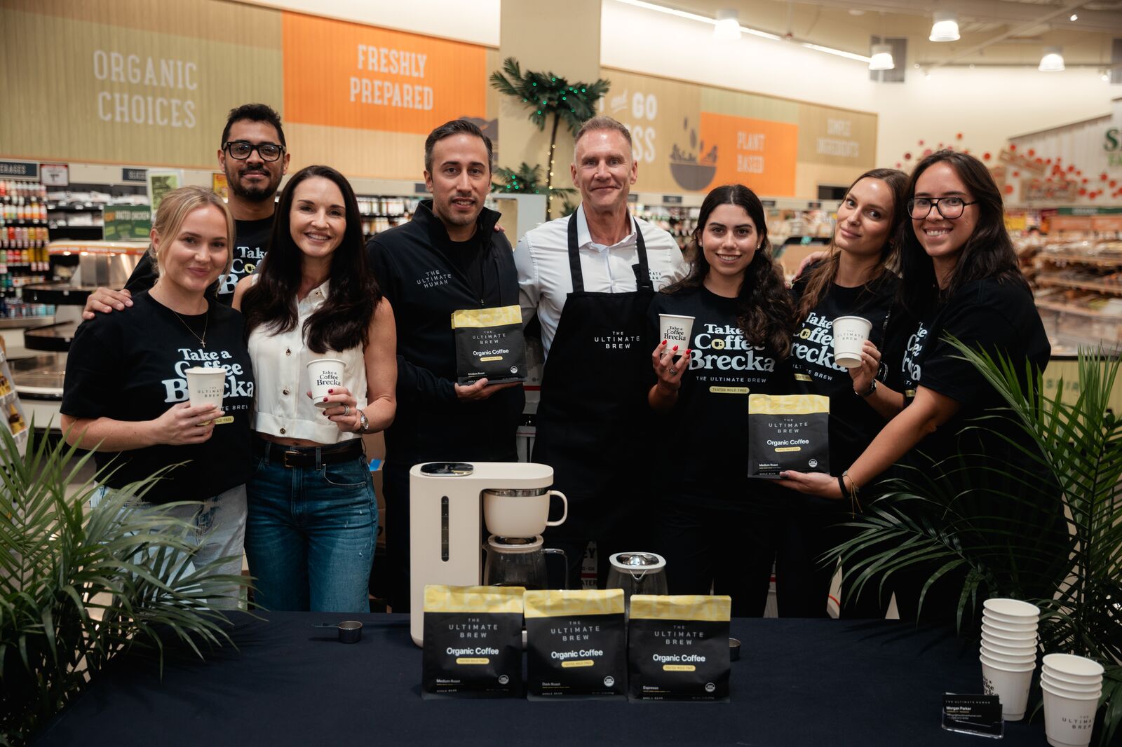 Gary Brecka and the Coffee Brecka team at the table, holding bags and cups of The Ultimate Brew